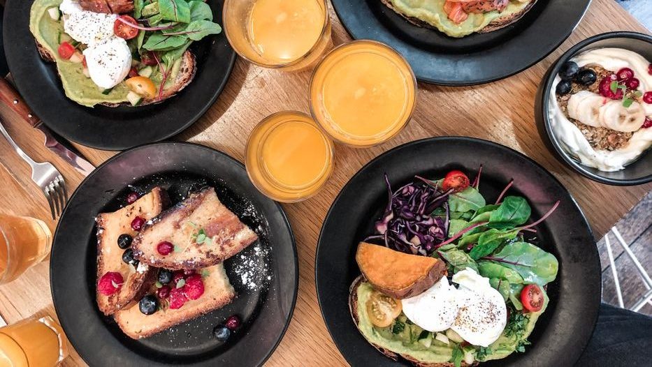 Top-down view of a vibrant brunch spread featuring avocado toast, salmon, fresh salad, and juice.